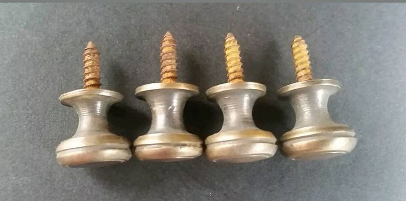 May include: Four antique brass screw-in knobs with a rounded top and a single screw. The knobs are a light brass colour with a slightly aged patina.