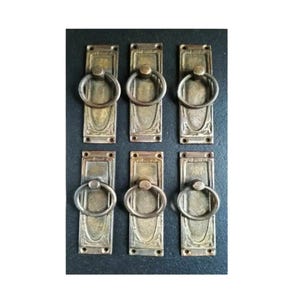 May include: Six antique brass drawer pulls with ornate designs and ring handles. The pulls are rectangular and have a slightly aged finish.