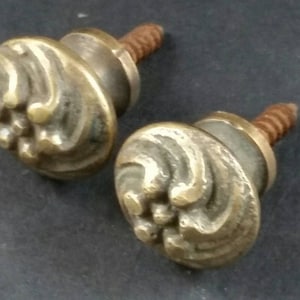 May include: Two antique brass cabinet knobs with a decorative swirl design and a screw on the back.