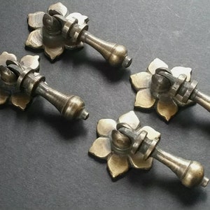 May include: Four antique brass drawer pulls with a floral design. Each pull has a round knob and a decorative base.