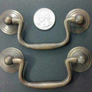 May include: Two antique brass drawer pulls with a rounded, decorative knob and a curved handle. The pulls are approximately 3 inches in length.