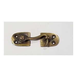 May include: A brass hook and eye latch with a curved hook and a rectangular plate with two holes. The latch is in a closed position.
