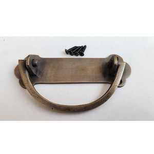 Op de afbeelding: Antiek messing ladetrekker met een rechthoekige plaat en een gebogen handvat. De trekker wordt geleverd met vier schroeven.