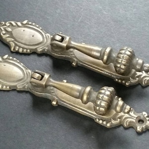 May include: Two ornate brass drawer pulls with a decorative floral design and a round knob. The pulls have a vintage look and would be a great addition to any home decor project.