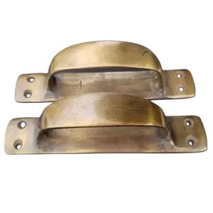 May include: Two antique brass door pulls with a rectangular base and a curved handle. The pulls are made of solid brass and have a polished finish.