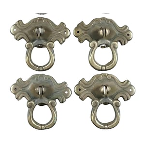 Op de afbeelding: Set van vier antieke messing kastgrepen met sierlijke ontwerpen en een ringgreep. Elke greep heeft een decoratieve, gegolfde rand en een ringgreep.