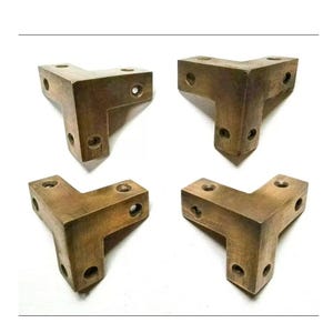 May include: Four brass corner brackets with four holes each. The brackets are in a T-shape and have a worn, aged look.