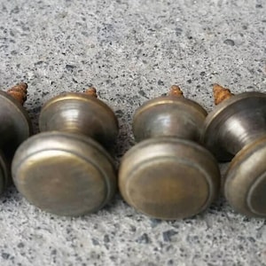 May include: Seven antique brass cabinet knobs with a rounded top and a screw on the back. The knobs have a worn, aged look.