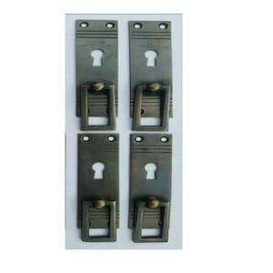 Peut inclure: Quatre poignées de porte d'armoire en laiton antique avec découpes de trous de serrure et une poignée de traction rectangulaire. Les poignées ont une finition vieillie et sont conçues dans un style vintage.