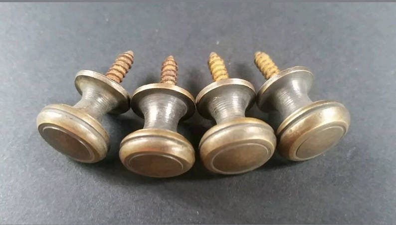 May include: Four brass cabinet knobs with a screw thread. Each knob has a round, slightly domed top with a raised edge.