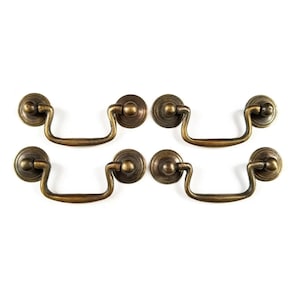 May include: Set of four antique brass cabinet pulls with a simple, elegant design. Each pull features a rounded, decorative knob and a curved, open handle.