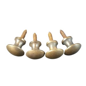 Puede incluir: Cuatro pomos de latón con tornillos. Los pomos son redondos y tienen un centro ligeramente elevado. Los tornillos son plateados.