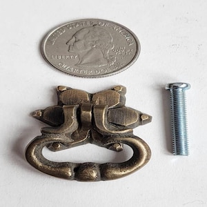 May include: A brass cabinet pull with a decorative design and a matching screw. The pull is about the size of a 25 pence coin.