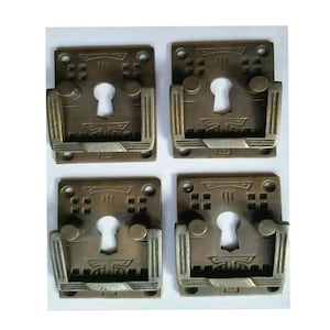 May include: Set of four antique brass cabinet pulls with a keyhole design. Each pull has a square base with a decorative pattern and a rectangular handle.