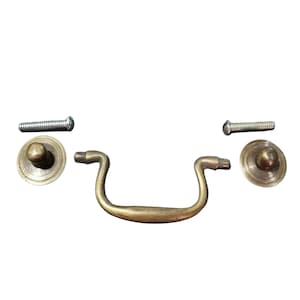 Puede incluir: Un tirador de cajón de latón con un asa curva y dos tornillos. El tirador tiene un pomo redondeado en cada extremo.