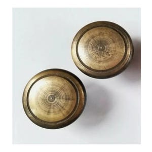 May include: Two round, brass knobs with a concentric circle design. The knobs have a slightly aged, antique look.