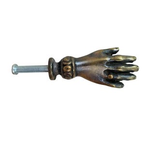 May include: A bronze hand-shaped cabinet knob with a decorative detail on the wrist and a screw for installation.