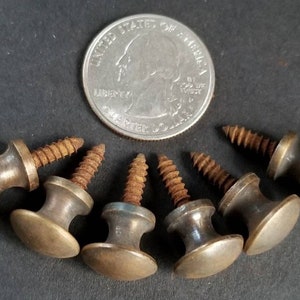 May include: Six antique brass knobs with screws. The knobs are round with a raised centre and a flat bottom. The screws are rusty.