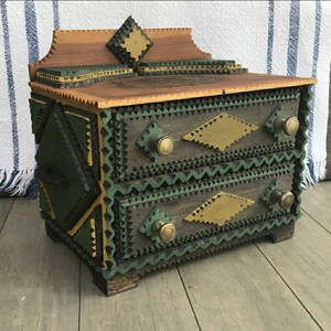 May include: A small wooden box with two drawers, intricately crafted with green and gold geometric patterns. The box has brass knobs and a decorative top.