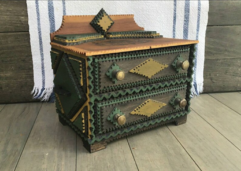 May include: A small wooden box with two drawers, intricately crafted with green and gold geometric patterns. The box has brass knobs and a decorative top.