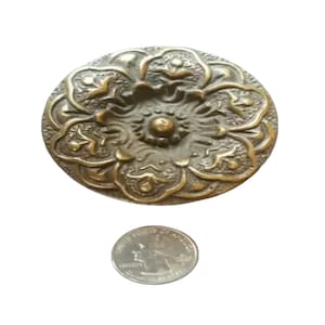May include: A round, brass, decorative door knob with a floral design. The knob is about the size of a UK 20 pence coin.