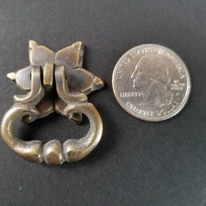 May include: A brass cabinet pull with a star-shaped design and a loop handle. The pull is about the size of a UK 20 pence coin.