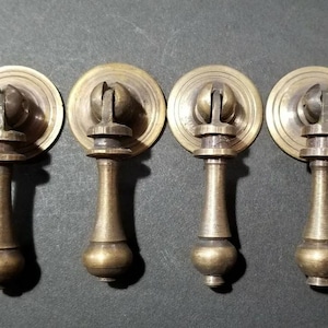 May include: Four antique brass cabinet knobs with a round, decorative top and a slender, tapered stem. The knobs have a polished finish and a classic design.