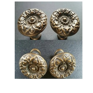 May include: Four antique bronze cabinet knobs with a floral design. The knobs have a round shape with intricate detailing, and a dark bronze finish. The knobs are likely made of metal and are suitable for furniture restoration or decorative projects.