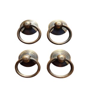 May include: Four antique brass cabinet door pulls with a ring handle and a round base.