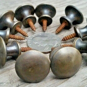May include: Ten antique brass cabinet knobs with screws. The knobs are round with a raised centre and a slightly oval shape. The screws are rusty.