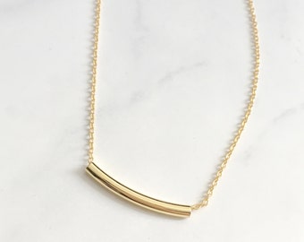 Puede incluir: Un collar de cadena de oro con un colgante de barra de oro curvado.