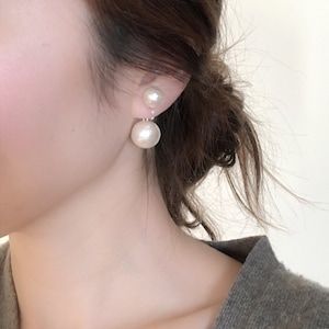 May include: A pair of pearl earrings with a larger pearl dangling below a smaller pearl. The earrings are worn by a person with brown hair.