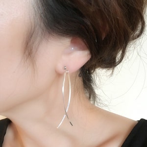 May include: Silver dangle earrings with a thin, curved design. The earrings are long and delicate.