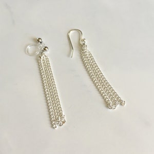 May include: A pair of silver chain earrings with a dangling design. One earring has a clip-on closure, while the other has a hook closure.