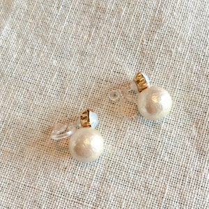May include: A pair of clip-on earrings with a pearl-like design. The earrings are made of a white material and have a gold-colored accent.
