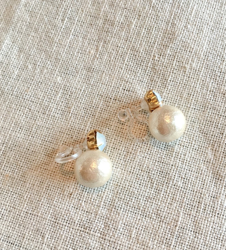 May include: A pair of clip-on earrings with a pearl-like design. The earrings are made of a white material and have a gold-colored accent.