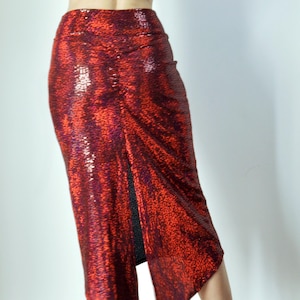 May include: A red sequined skirt with a high slit and a fitted silhouette. The skirt is worn by a person with black heels.