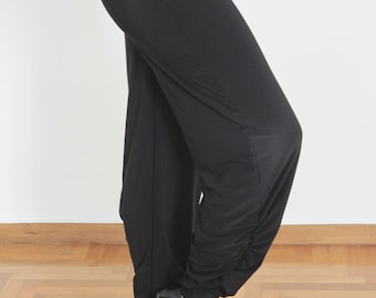 May include: Black dance pants with a gathered detail at the ankles. The pants are worn by a person wearing black heels. The word "Reina" is written in red cursive on a white background.