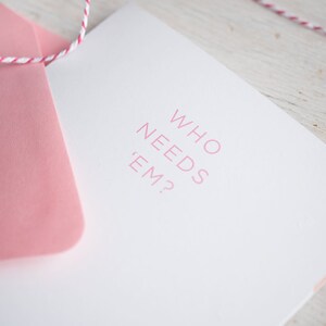 May include: A white card with a pink envelope. The card has the text "WHO NEEDS 'EM?" printed in pink.