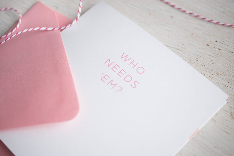 May include: A white card with a pink envelope. The card has the text "WHO NEEDS 'EM?" printed in pink.