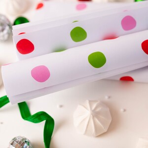 May include: White wrapping paper with red, green, and pink polka dots. The paper is rolled up and stacked on a white surface.