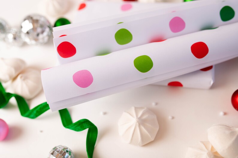 May include: White wrapping paper with red, green, and pink polka dots. The paper is rolled up and stacked on a white surface.