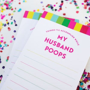 May include: A notepad with a colorful striped border and the text "Things I'll Accomplish While My Husband Poops" in pink letters. The notepad has lined pages for writing.