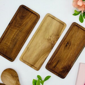 May include: Three rectangular wooden serving trays in various shades of brown. The trays are made of natural wood and have a rustic, handcrafted look.