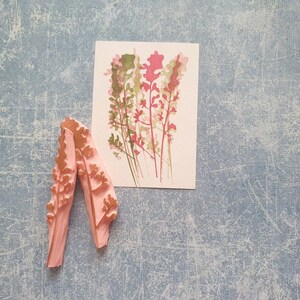 May include: Two pink rubber stamps with a floral design. The stamps are shaped like a long, thin leaf with a pointed tip. The design is of a cluster of pink and green flowers.