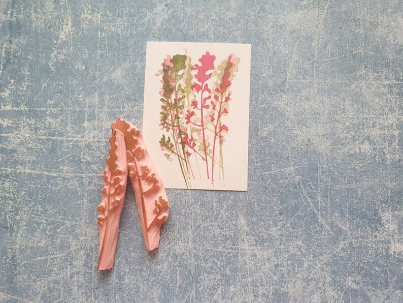 May include: Two pink rubber stamps with a floral design. The stamps are shaped like a long, thin leaf with a pointed tip. The design is of a cluster of pink and green flowers.