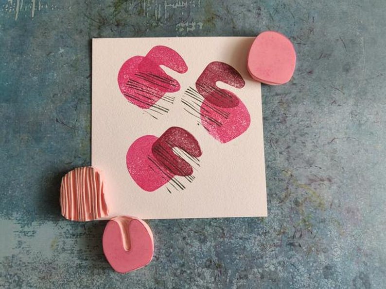 May include: A square card with three pink abstract shapes with black lines, and three pink erasers. The shapes on the card are in a heart-like form. The erasers are in different shapes.