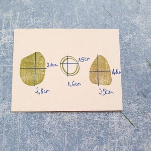 May include: Three shapes drawn on a beige paper background. The shapes are outlined in black and filled in with a light green color. The shapes are labeled with measurements in centimeters.