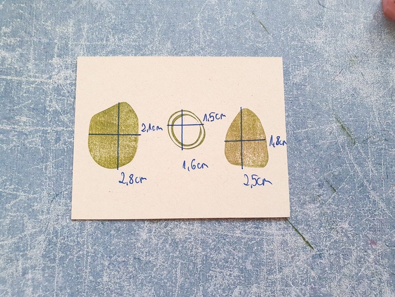 May include: Three shapes drawn on a beige paper background. The shapes are outlined in black and filled in with a light green color. The shapes are labeled with measurements in centimeters.