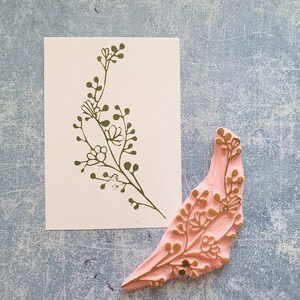 May include: A pink rubber stamp with a gold floral design. The stamp is shaped like a leaf and has a detailed floral pattern.